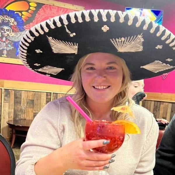 Smiling woman in a sombrero holding a red drink with an orange slice and umbrella.