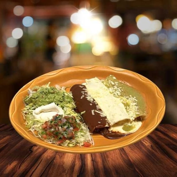 A plate of enchiladas with green and mole sauces, topped with cheese, guacamole, and pico de gallo.
