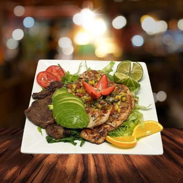 Grilled chicken and steak with avocado, salsa, tomatoes, and limes on a white plate.
