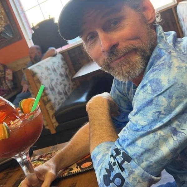 Man in a blue shirt and cap smiles at the camera, holding a large drink with an inverted bottle.