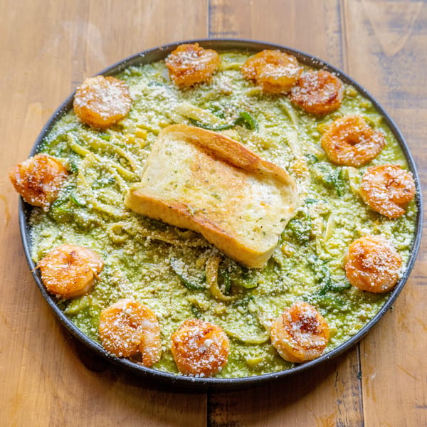 Pesto pasta with shrimp and garlic bread, sprinkled with parmesan cheese on a wooden table.