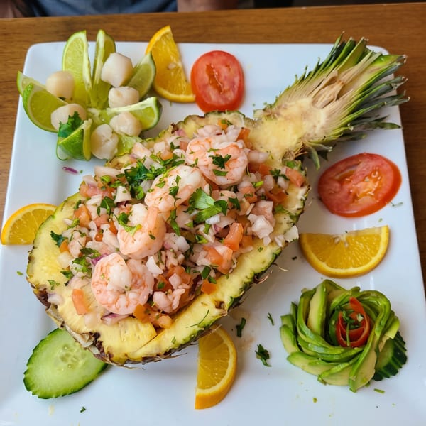 Shrimp ceviche served in a pineapple half, garnished with lime, orange, tomato, cucumber, and avocado.