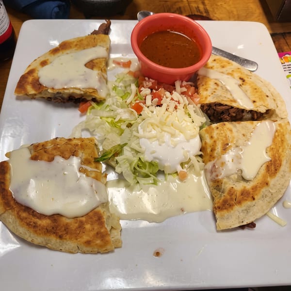 Four quesadilla slices with white cheese sauce, a side salad, sour cream, and salsa.