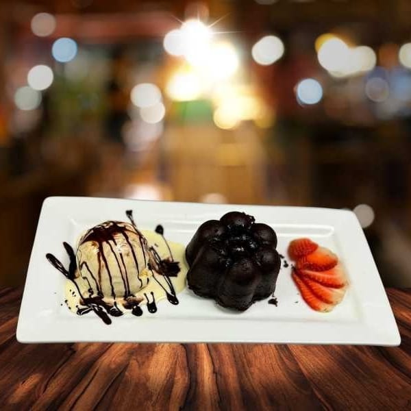 Chocolate lava cake with vanilla ice cream drizzled in chocolate sauce and sliced strawberries.