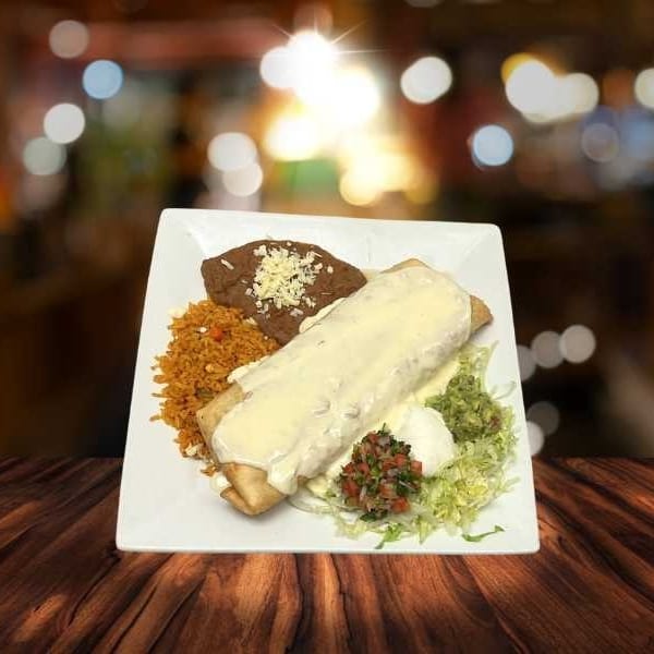 A large burrito covered in white cheese sauce, with rice, beans, guacamole, and pico de gallo.