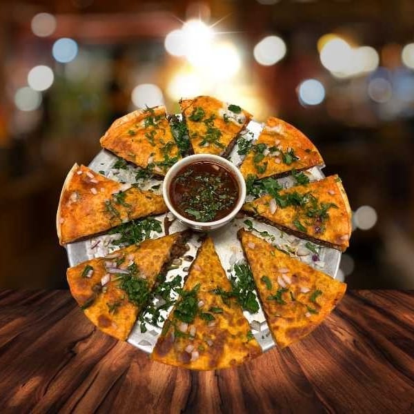 A round flatbread pizza, cut into slices, with a dipping sauce in the center.
