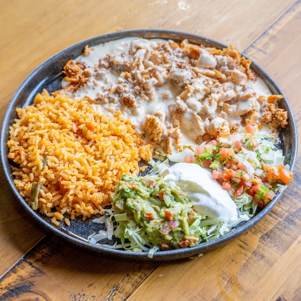 A Mexican dish with rice, chicken covered in white sauce, guacamole, sour cream, and pico de gallo.
