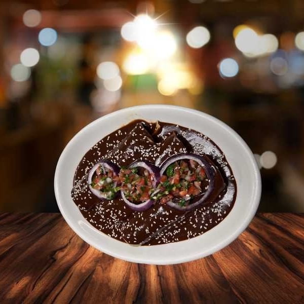 Mole enchiladas topped with red onion rings and pico de gallo, on a wooden table.