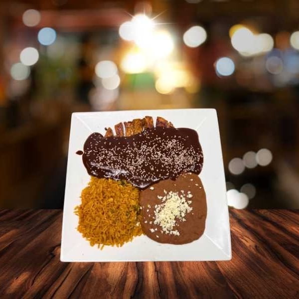 A plate of chicken mole with rice and refried beans, topped with cheese, on a wooden table.