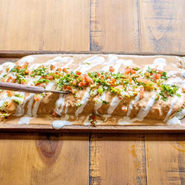A large burrito covered in creamy sauce, pico de gallo, and cilantro, with a knife cutting into it.