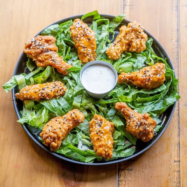 Crispy chicken wings with sesame seeds and dipping sauce on a bed of lettuce.