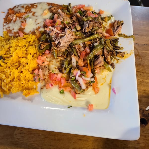 A white plate with yellow rice, refried beans with cheese, and shredded meat with vegetables.