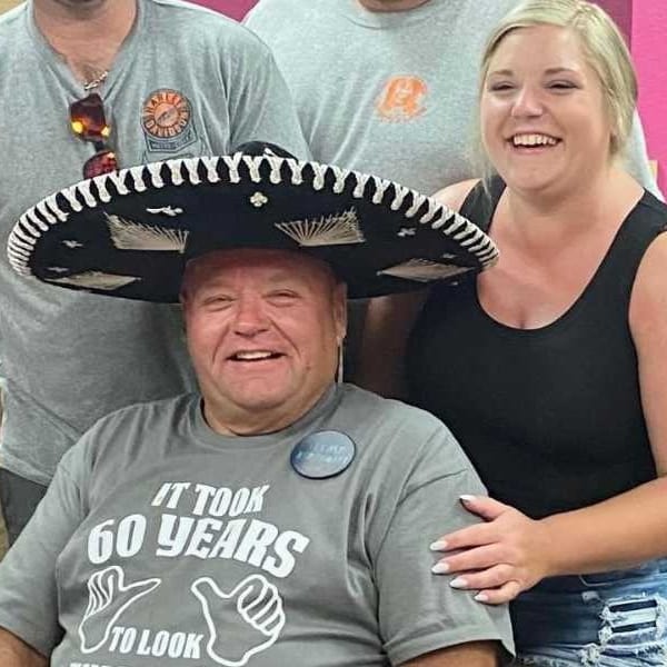 Man in a sombrero and "It Took 60 Years" shirt, smiling with friends at a party.